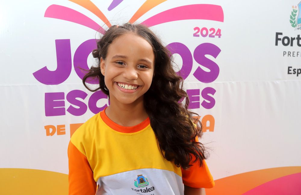 criança com farda da rede de ensino municipal sorri posando para a foto